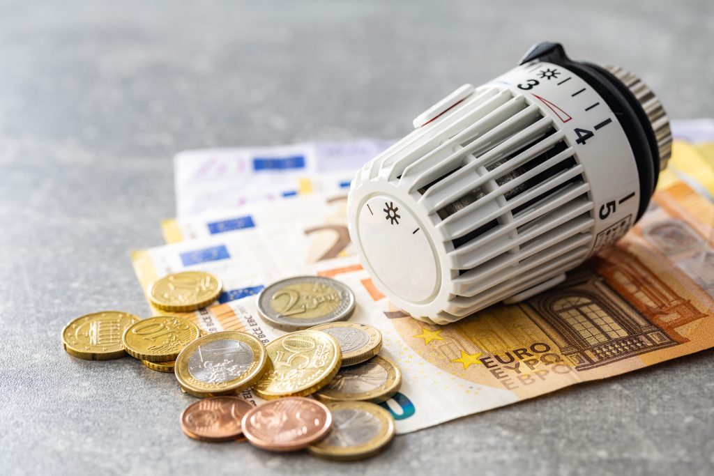Heizthermostat auf Euro-Banknoten und Münzen – Symbol für Heizkosten und Energieeinsparung